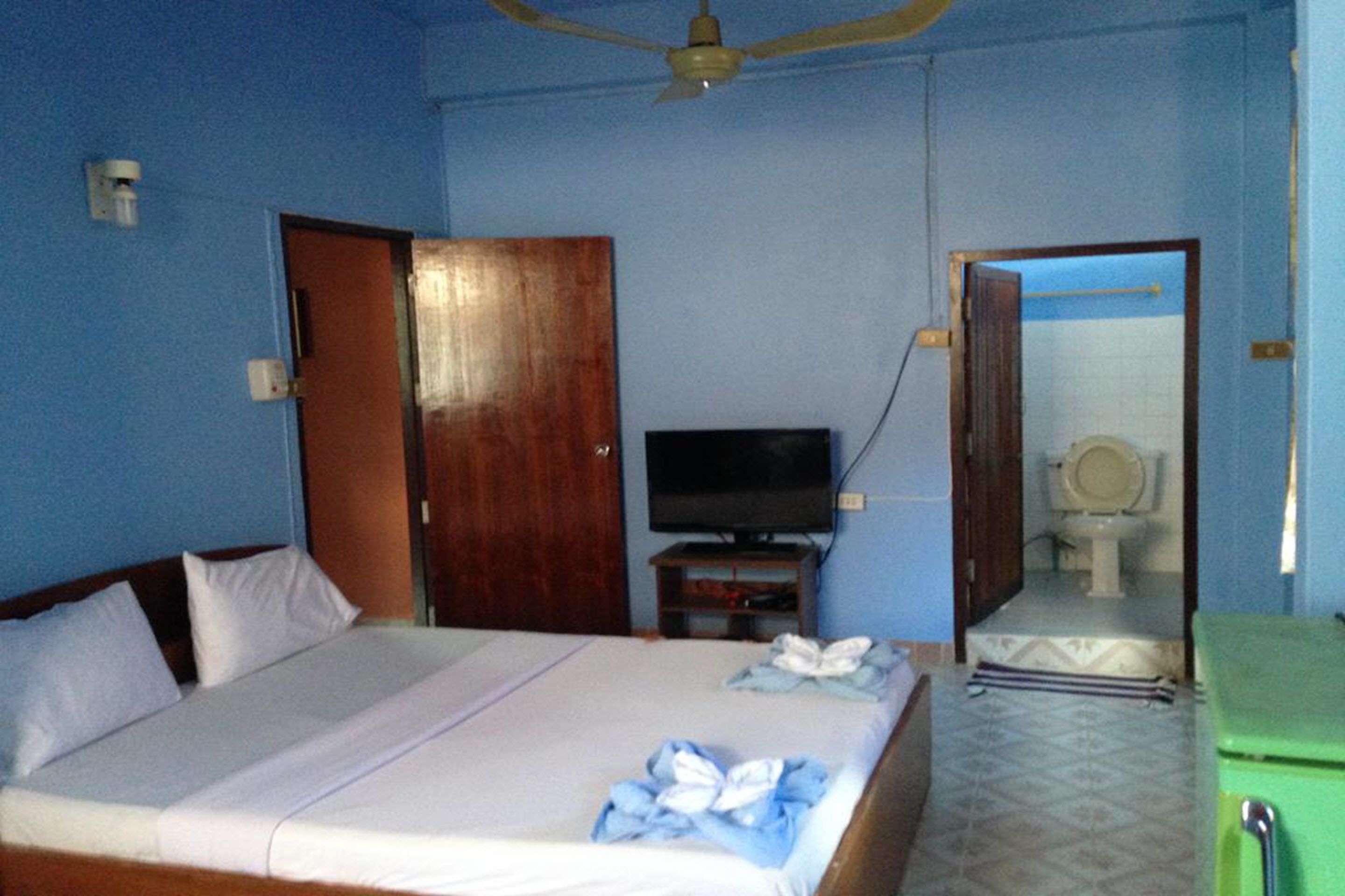 Una habitación con una cama, televisión, espejo y un armario verde.