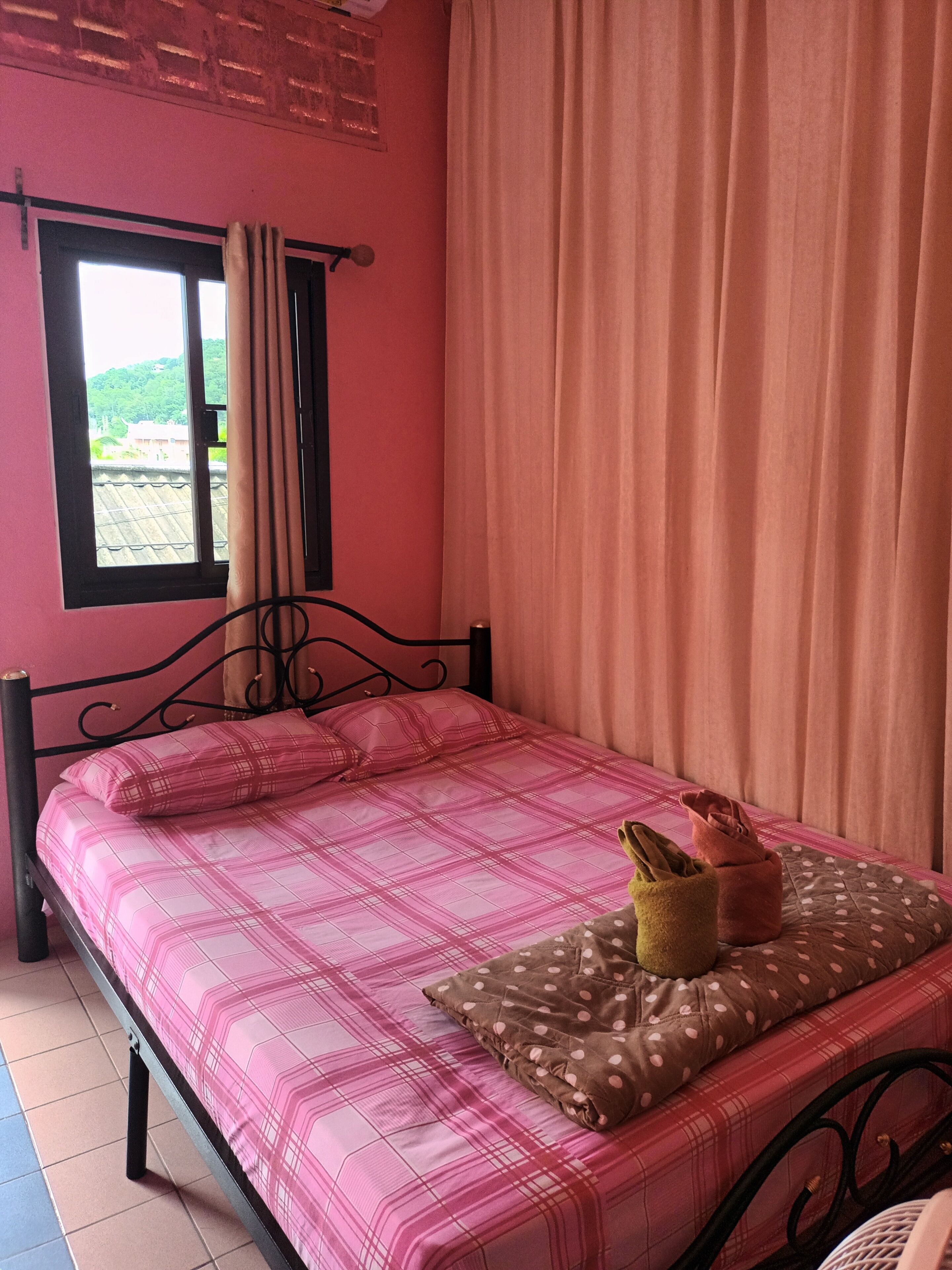 Ein Zimmer mit einem Bett, einem fensterbelaubten Fenster und Blick auf Grün.