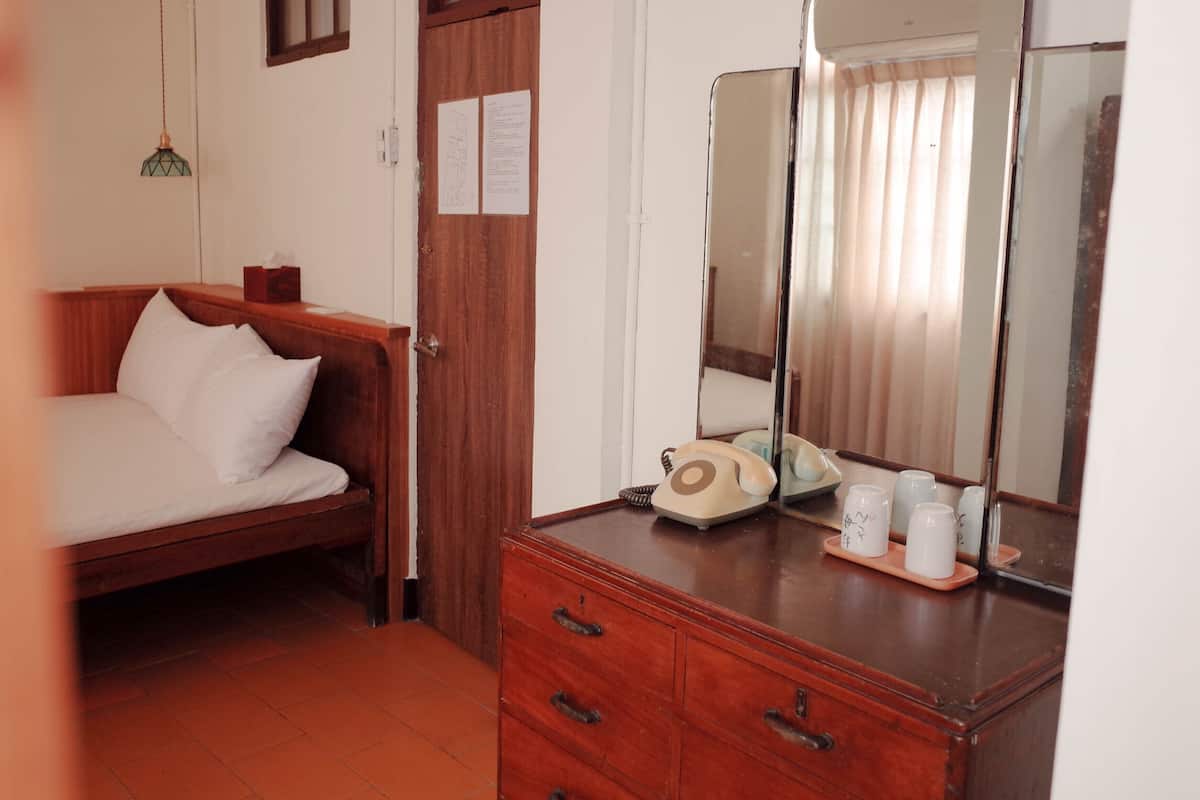 A bedroom with a wooden bed, a dresser with a mirror, and a telephone.