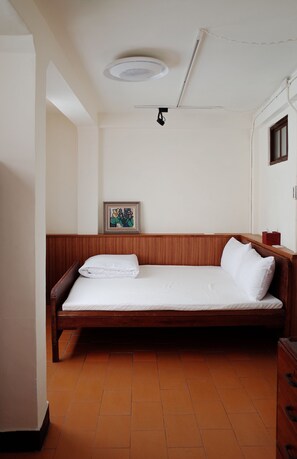 Una cama individual con cabecera de madera, colchón blanco y mesita de noche con lámpara.