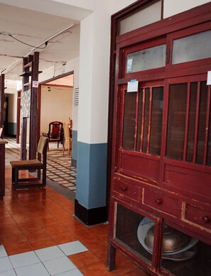 Un pasillo con suelo de baldosas, un banco de madera y una puerta roja con un cuenco de metal.