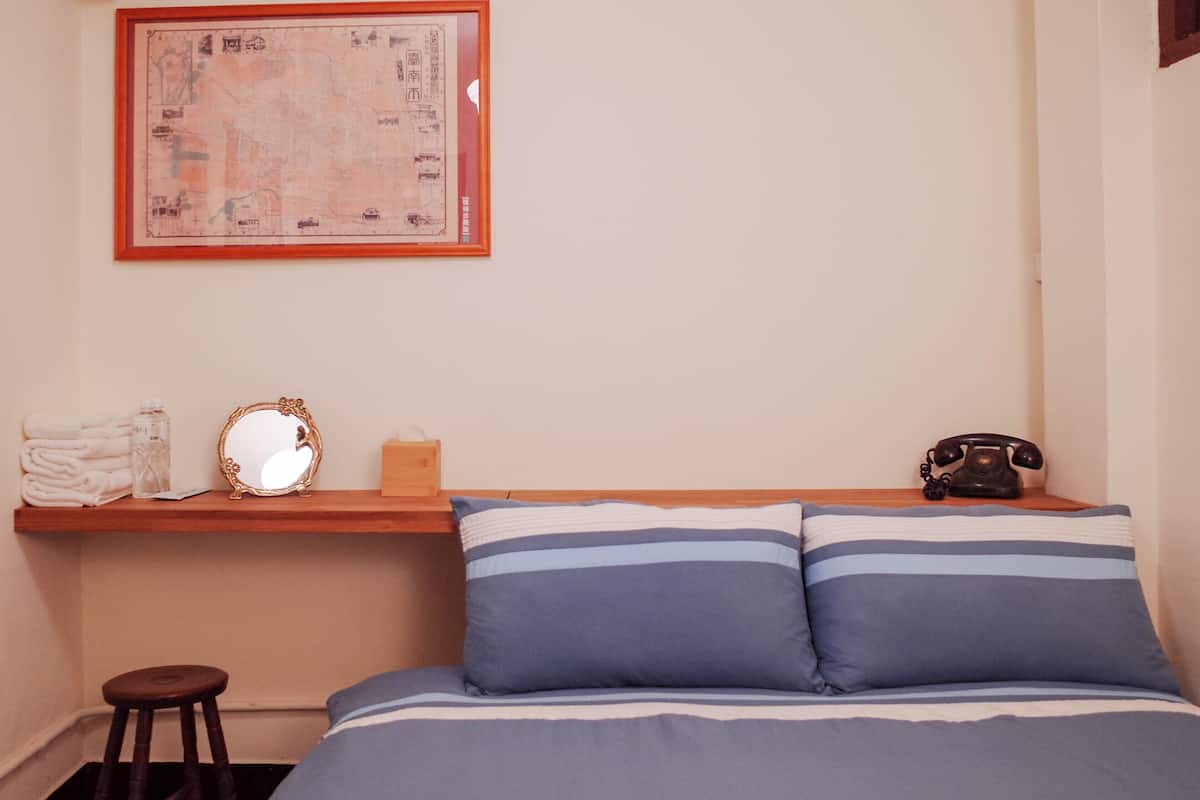 A bedroom with a bed, a map on the wall, a telephone, and a small stool.