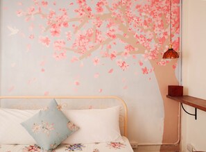 Un dormitorio con cama, almohadas, una pared con un mural floral, una lámpara colgante y un estante de madera.