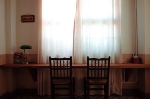 Una habitación con escritorio, dos sillas, lámpara e imagen en la pared.