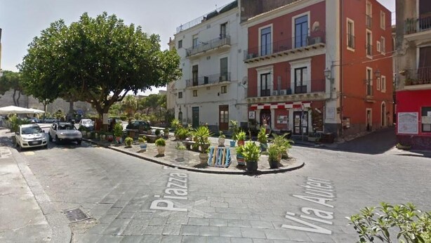 Une rue bordée d’immeubles, avec un arbre et des voitures garées.