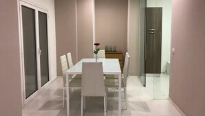 Un espace repas moderne avec une table et des chaises blanches, un vase avec une fleur et une cloison en verre.