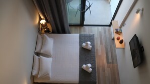 Una habitación de hotel con cama, lámparas de noche, una mesita con lámpara, una ventana con vistas y un cuadro colgado en la pared.