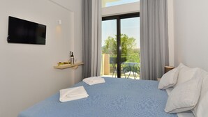Habitación de hotel con una cama, un televisor de pantalla plana montado en la pared, una mesita con una botella y vasos, y vistas al exterior a través de un ventanal grande.