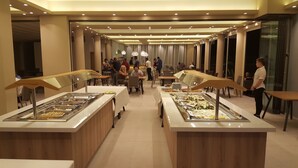 Un área de bufé con varias estaciones de comida, mesas y sillas dispuestas en un amplio salón.