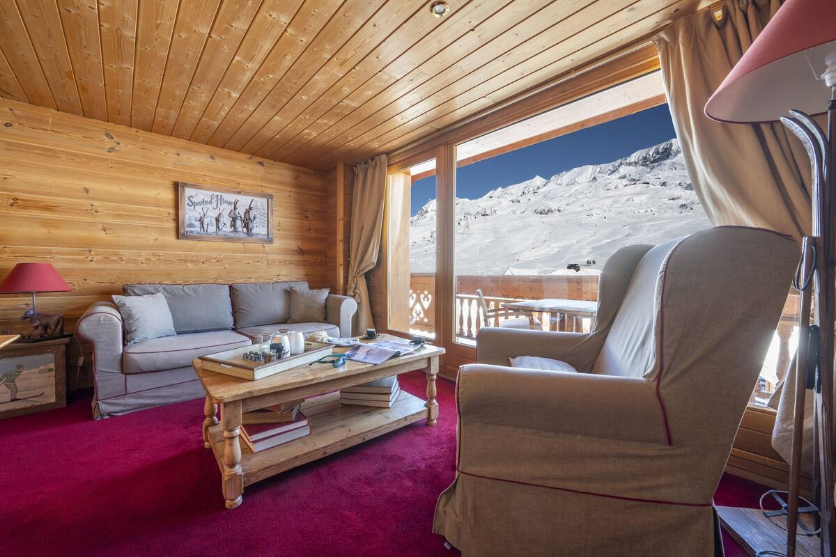 Une pièce chaleureuse, avec des murs en bois, un canapé, un fauteuil et une table sur laquelle sont posés des livres et une lampe.