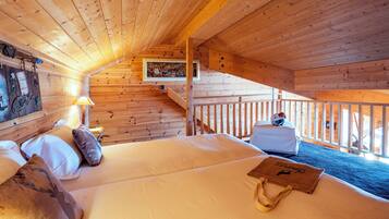 Acogedora habitación de cabaña de madera con cama, almohadas, una mesita de noche, una lámpara, un cuadro enmarcado y una escalera que lleva a un balcón.
