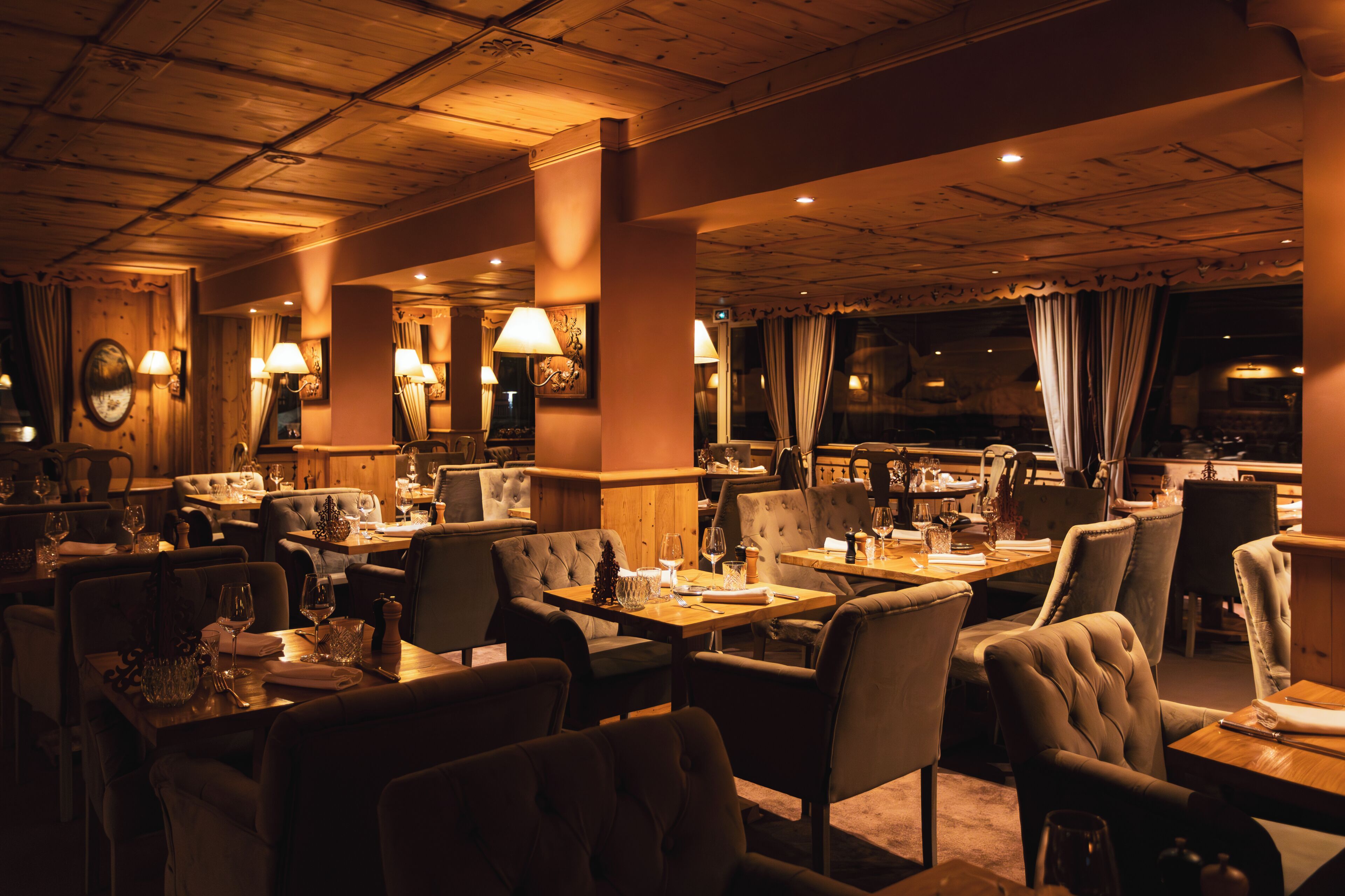 Ein schwach beleuchtetes Restaurant mit Holzvertäfelung, mehreren Tischen und Stühlen.