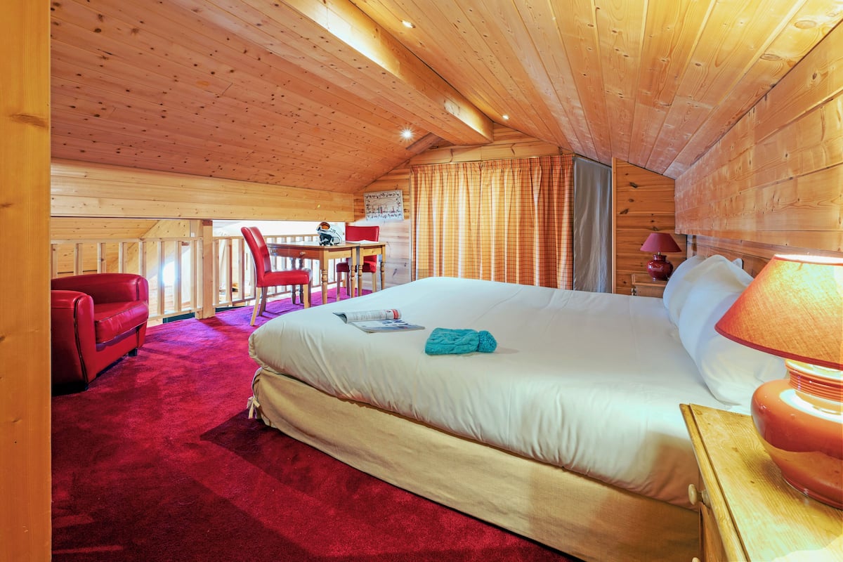 Une pièce confortable avec un grand lit, un canapé rouge, une table en bois et une fenêtre avec des rideaux.