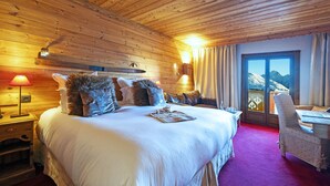 Un dormitorio con paneles de madera, una cama grande, un escritorio y vistas a la montaña a través de una puerta de cristal.