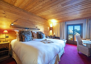 Un dormitorio con paneles de madera, una cama grande, un escritorio y vistas a la montaña a través de una puerta de cristal.