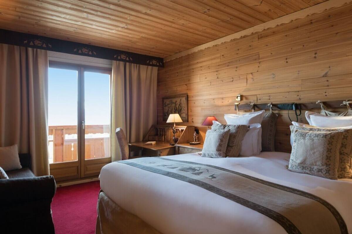 Une chambre d’hôtel avec un plafond en bois, un grand lit avec de nombreux oreillers, un bureau avec une lampe et une vue sur l’extérieur, accessible par une porte coulissante.