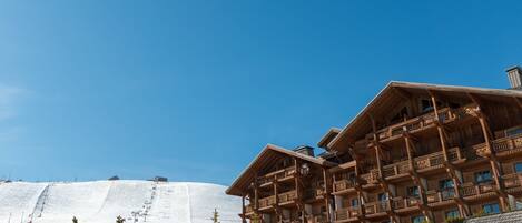 A wooden building with multiple balconies and a ski slope in the background.
