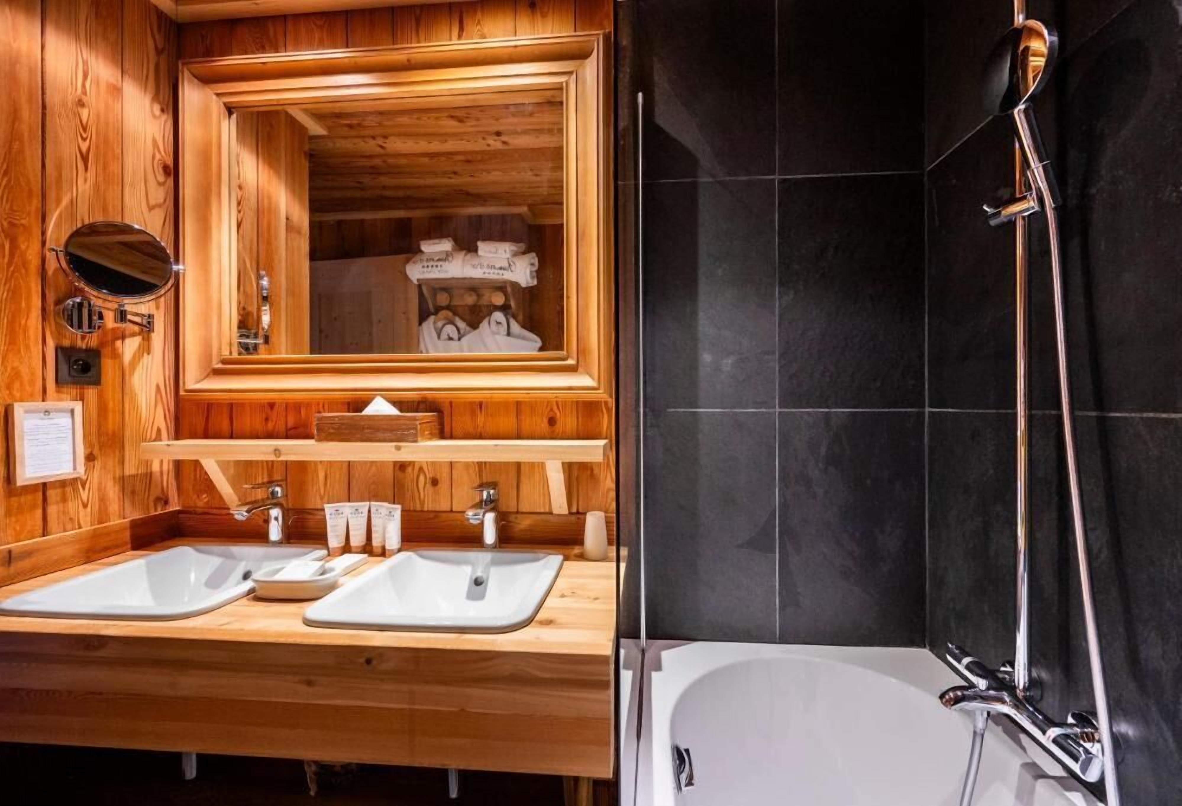 A wooden bathroom with two sinks, a mirror, and a shower.