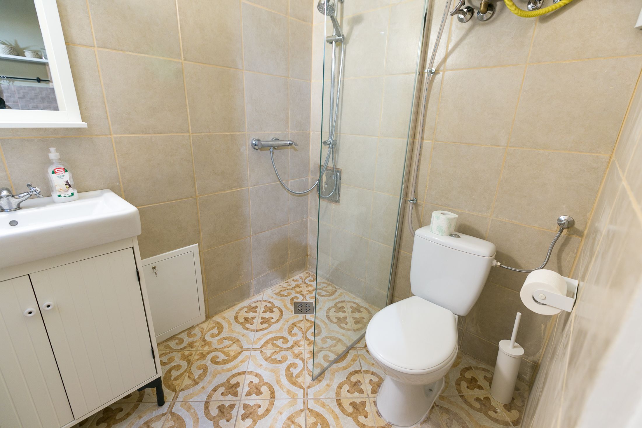 A bathroom with a shower, toilet, sink, and patterned floor tiles.