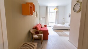 Habitación de hotel moderna con un sofá rojo, una silla de mimbre, una cama y un ventanal grande.