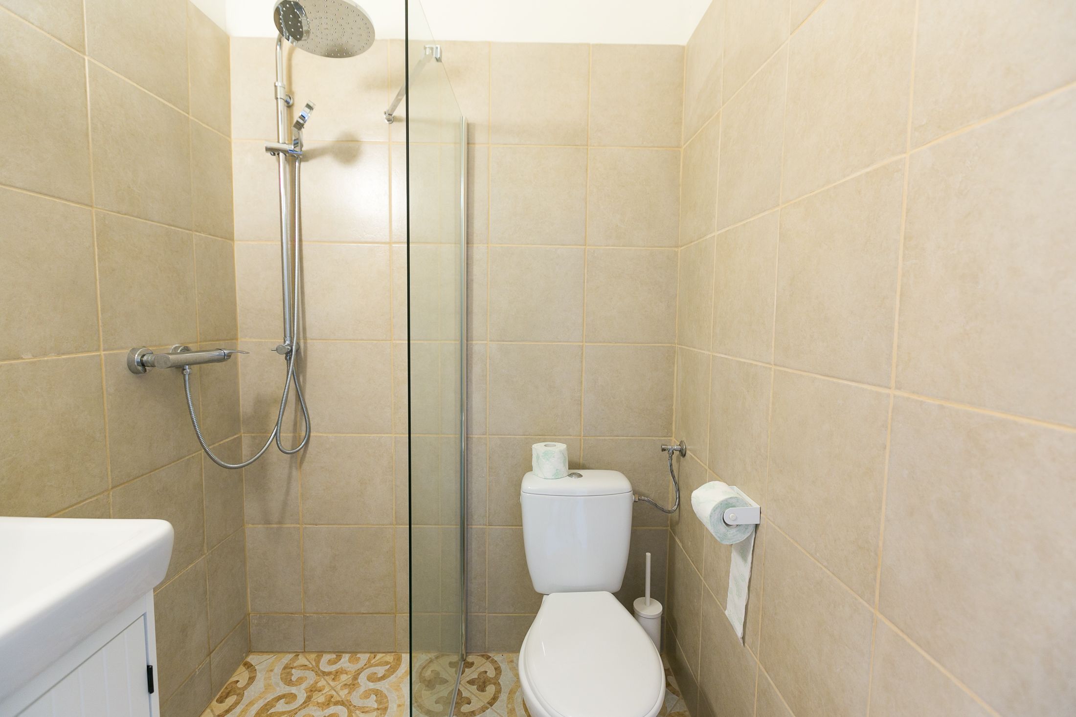A bathroom with a shower, toilet, and a patterned floor.