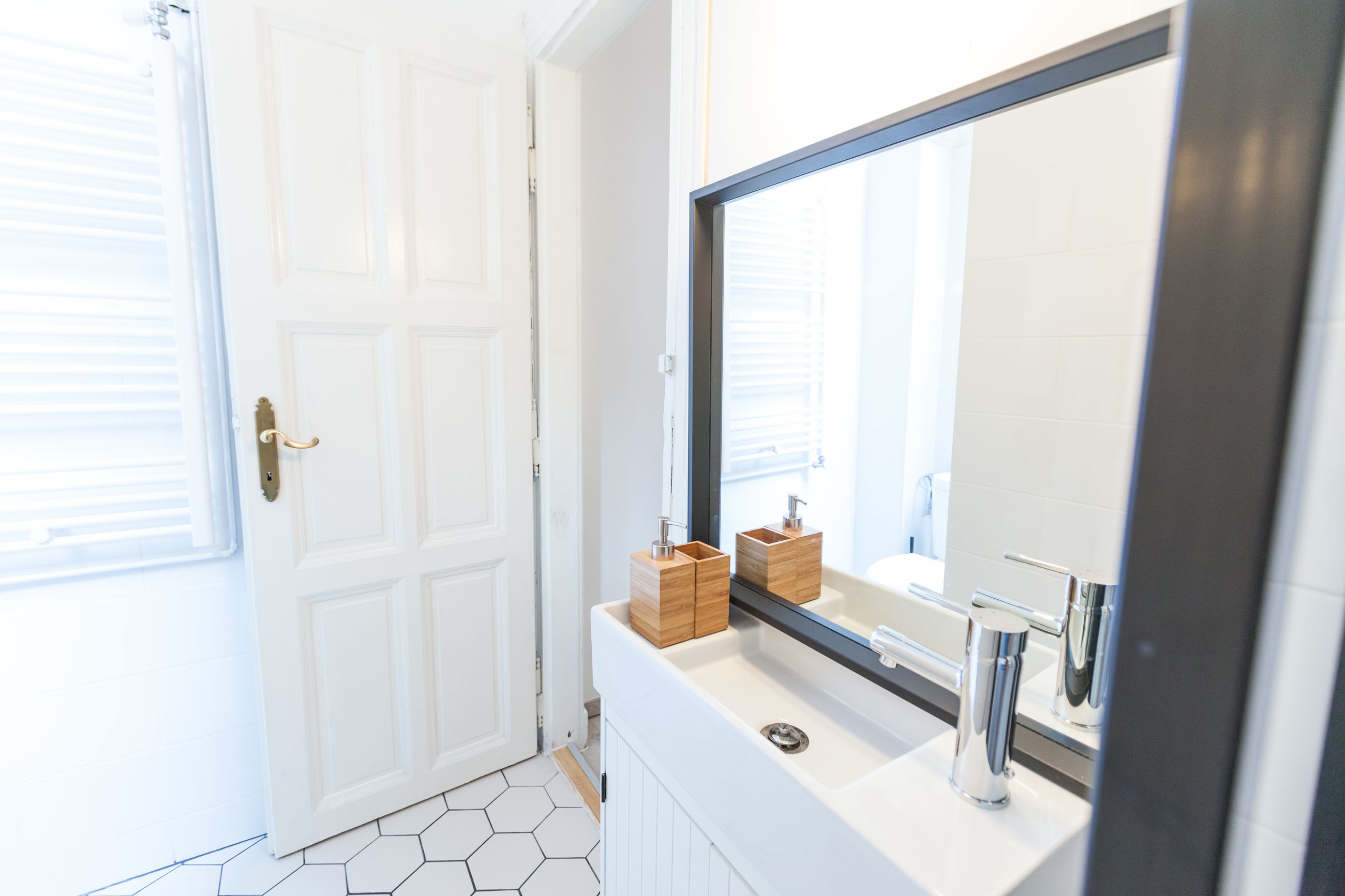 A bathroom with a white door, a large mirror, and a white sink with chrome fixtures.