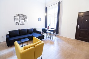 Un salon moderne avec un canapé bleu foncé, des fauteuils jaunes, une table à manger et une grande fenêtre avec des rideaux.