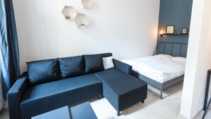 A modern room with a dark blue sectional sofa, a single bed, and a small white table. - Modern Ernesto II (Budapest)