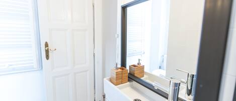 A bathroom with a white door, a large mirror, and a white sink with chrome fixtures.
