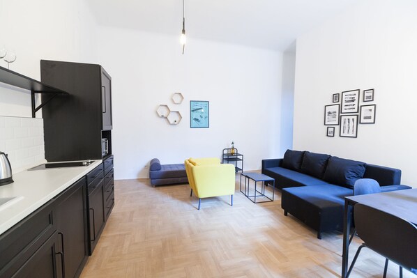 A modern kitchen with black cabinets and a white countertop, a yellow chair, a blue sofa, and a black dining table.