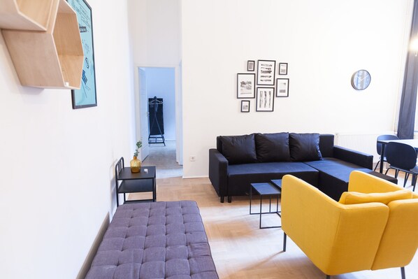 A modern living room with a sectional sofa, a yellow armchair, a small table, and a wall-mounted shelf.