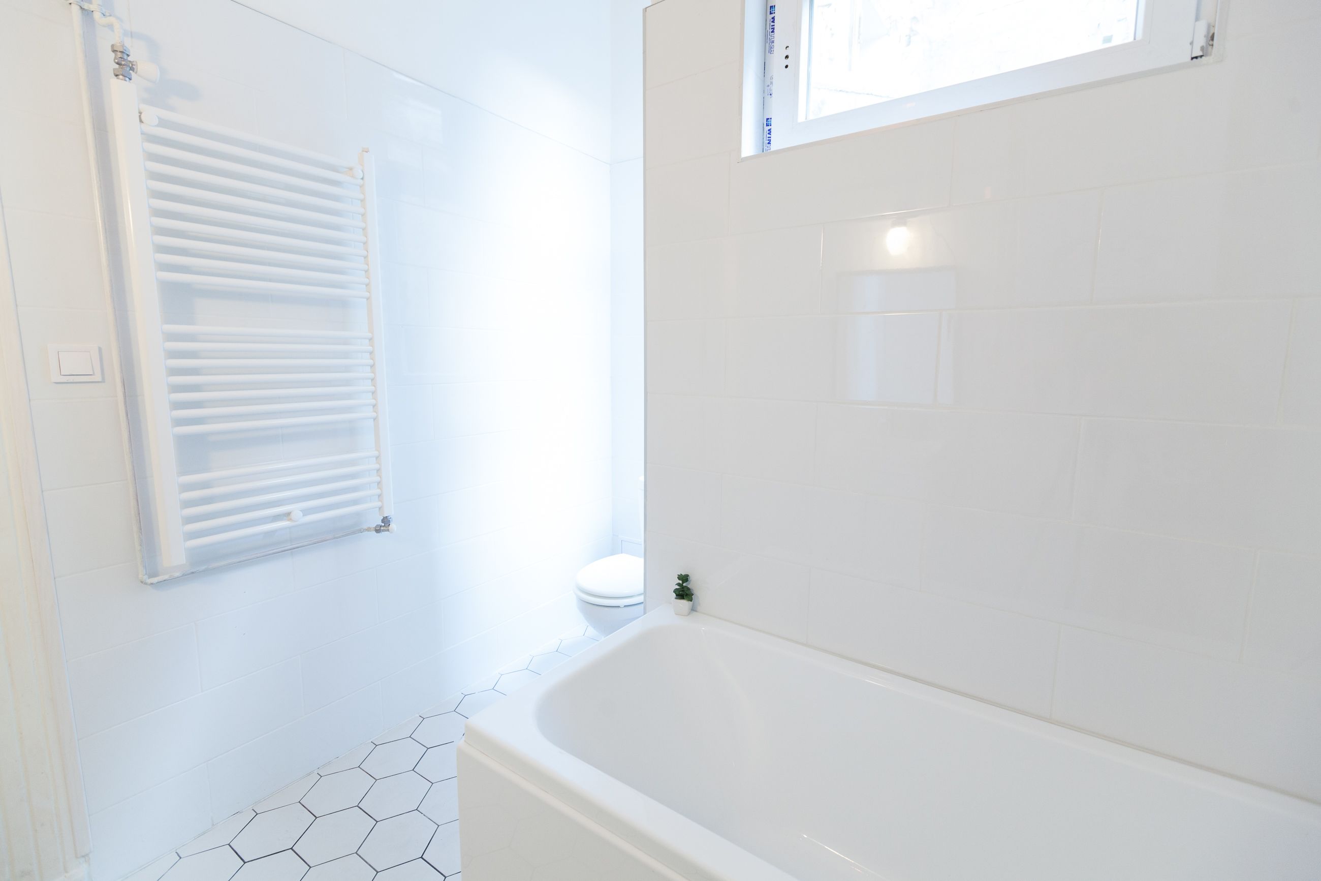 A bathroom with a white bathtub, a window with blinds, and a hexagonal tile floor.