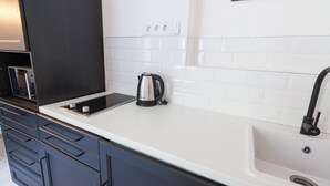 Cocina moderna con encimera blanca, armarios negros, hervidor y pileta.