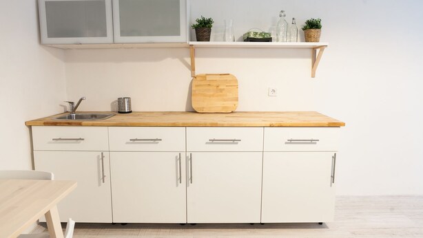 Una cocina con encimera de madera, armarios blancos y una repisa superior con botellas de vidrio y plantas.