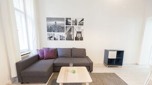 Un salón moderno con un sofá seccional gris, una pequeña mesa de centro de madera y una obra de arte con un paisaje urbano blanco y negro.
