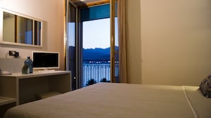 Hotelkamer met een bed, een bureau met een computer, een spiegel en een raam met uitzicht op bergen.