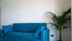 Een smaragdgroene bank met kussens, een potplant en een stopcontact op de muur.