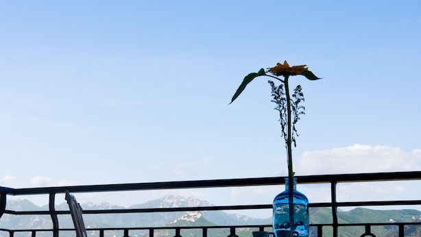 Een balkon met een metalen hekwerk, een tafel met een blauwe vaas, en een stoel.
