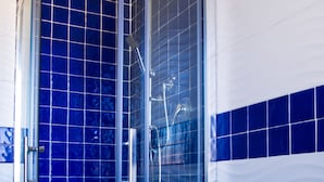 Een badkamer met een douchecabine van glas, een witte wastafel en blauwe betegelde wanden.