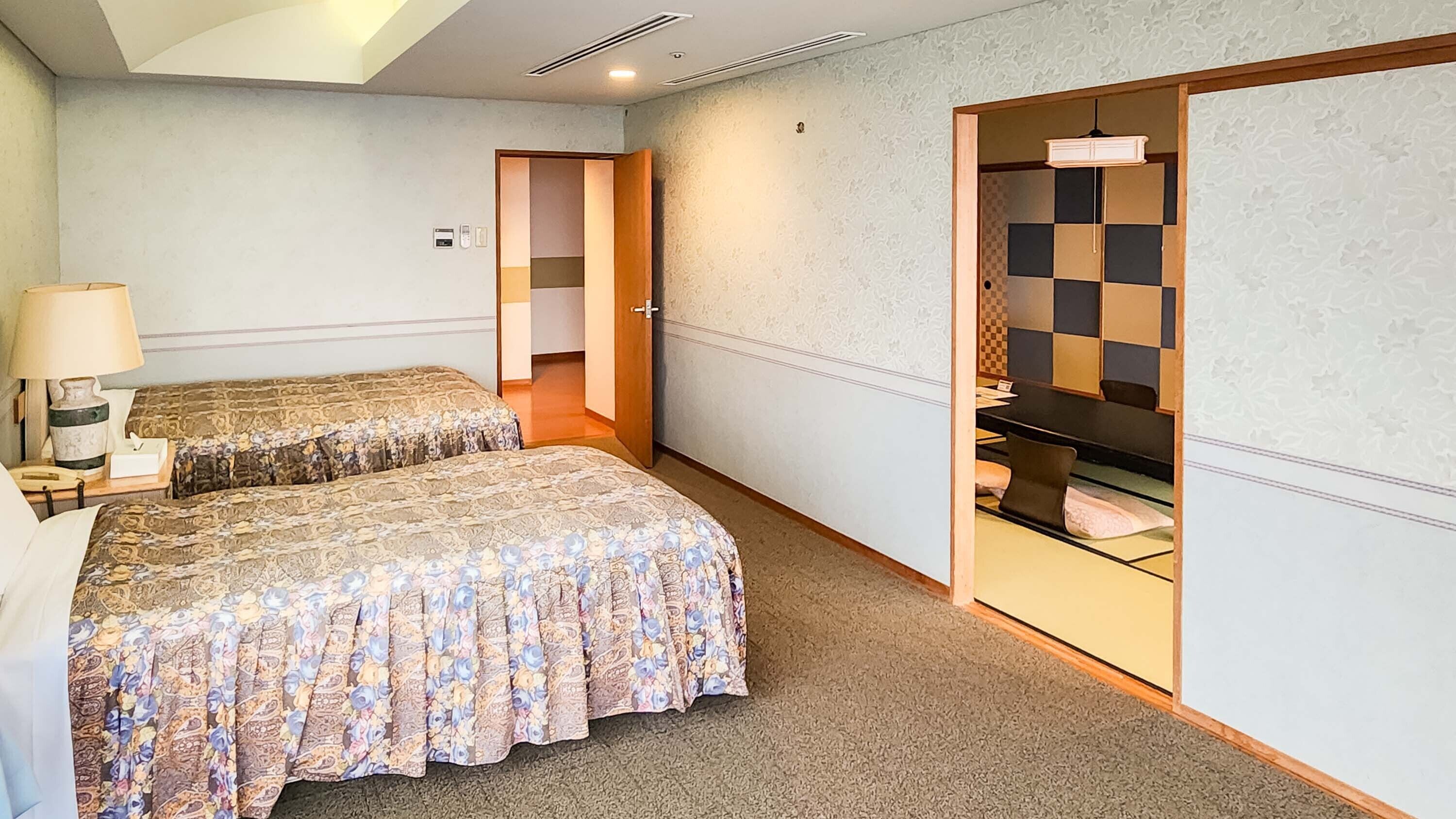 Ein Hotelzimmer mit zwei Betten, einem Schreibtisch, einer Lampe und einem durchgegangenen Tür erkennbaren Badezimmer.