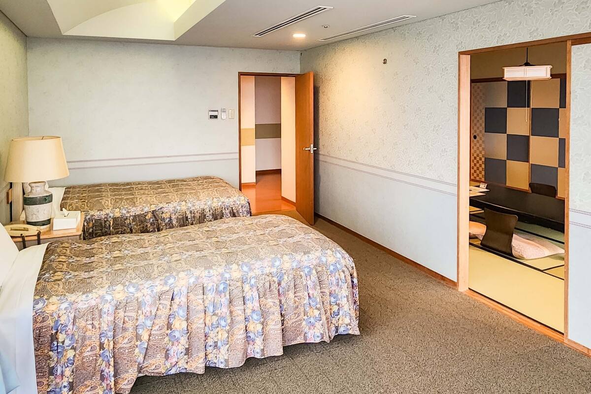 A hotel room with two beds, a desk, a lamp, and a bathroom visible through an open door.
