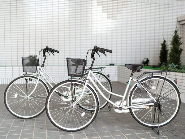 Two bicycles parked against a tiled wall with a metal fence and greenery in the background. - Hotel Cetus Royal (Higashiizu)