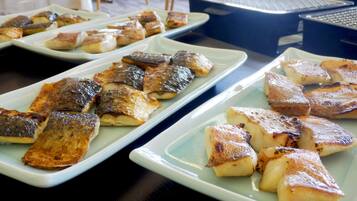 A buffet table with various dishes, including grilled fish and potatoes, arranged on rectangular plates.