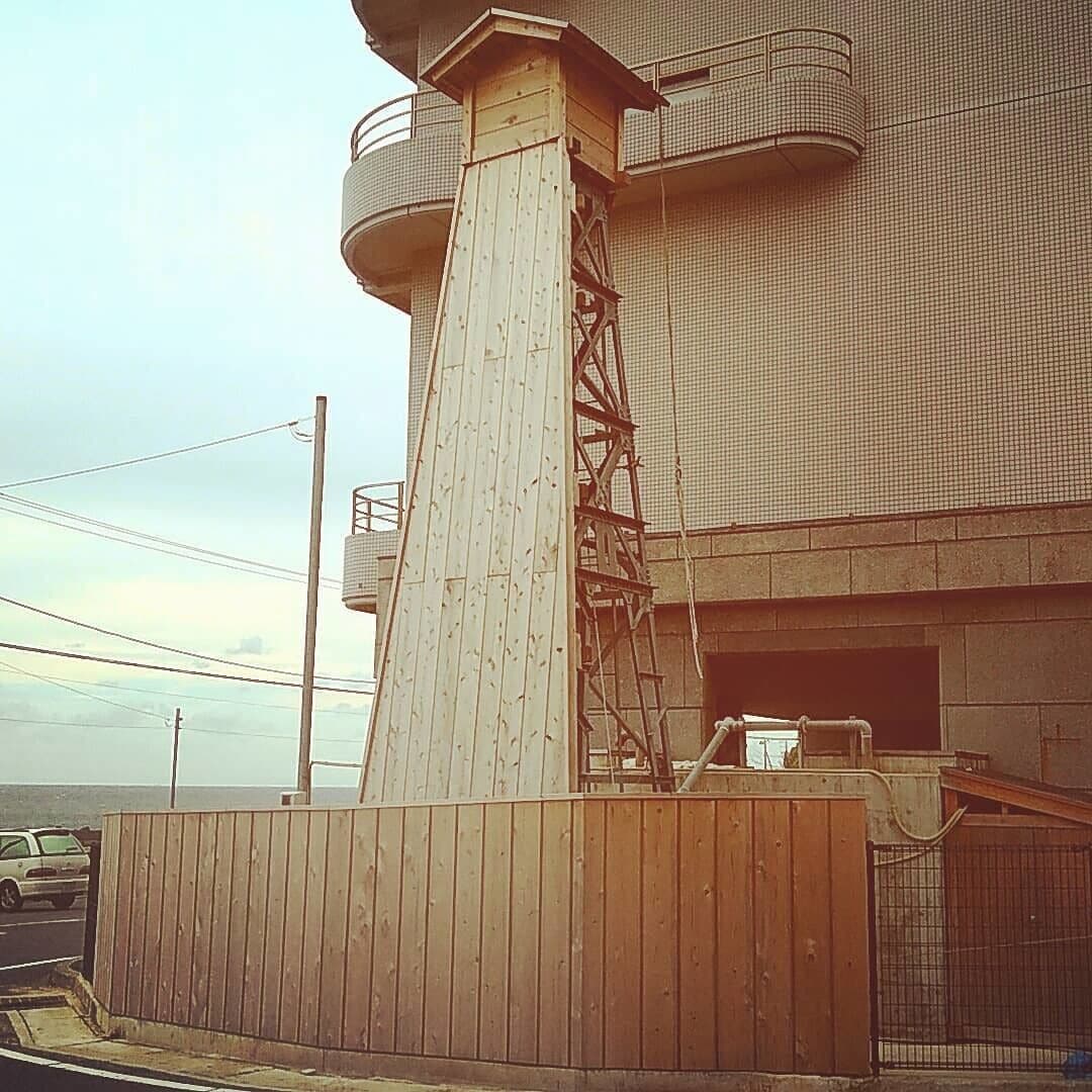Un edificio con una estructura alta y esbelta similar a una torre, un área cercada y un estacionamiento con un automóvil.