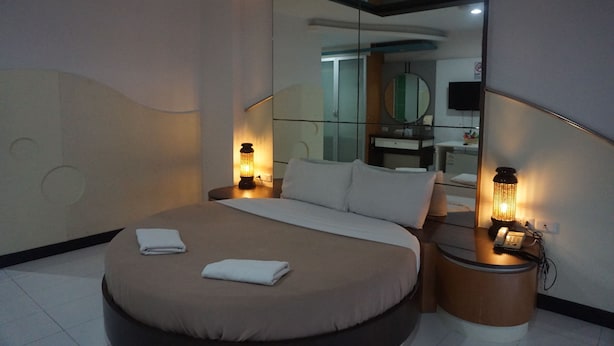 Una habitación de hotel moderna con una cama grande, dos lámparas de noche, un espejo y una mesita con un teléfono.