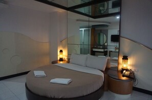 A modern hotel room with a large bed, two bedside lamps, a mirror, and a small table with a phone.