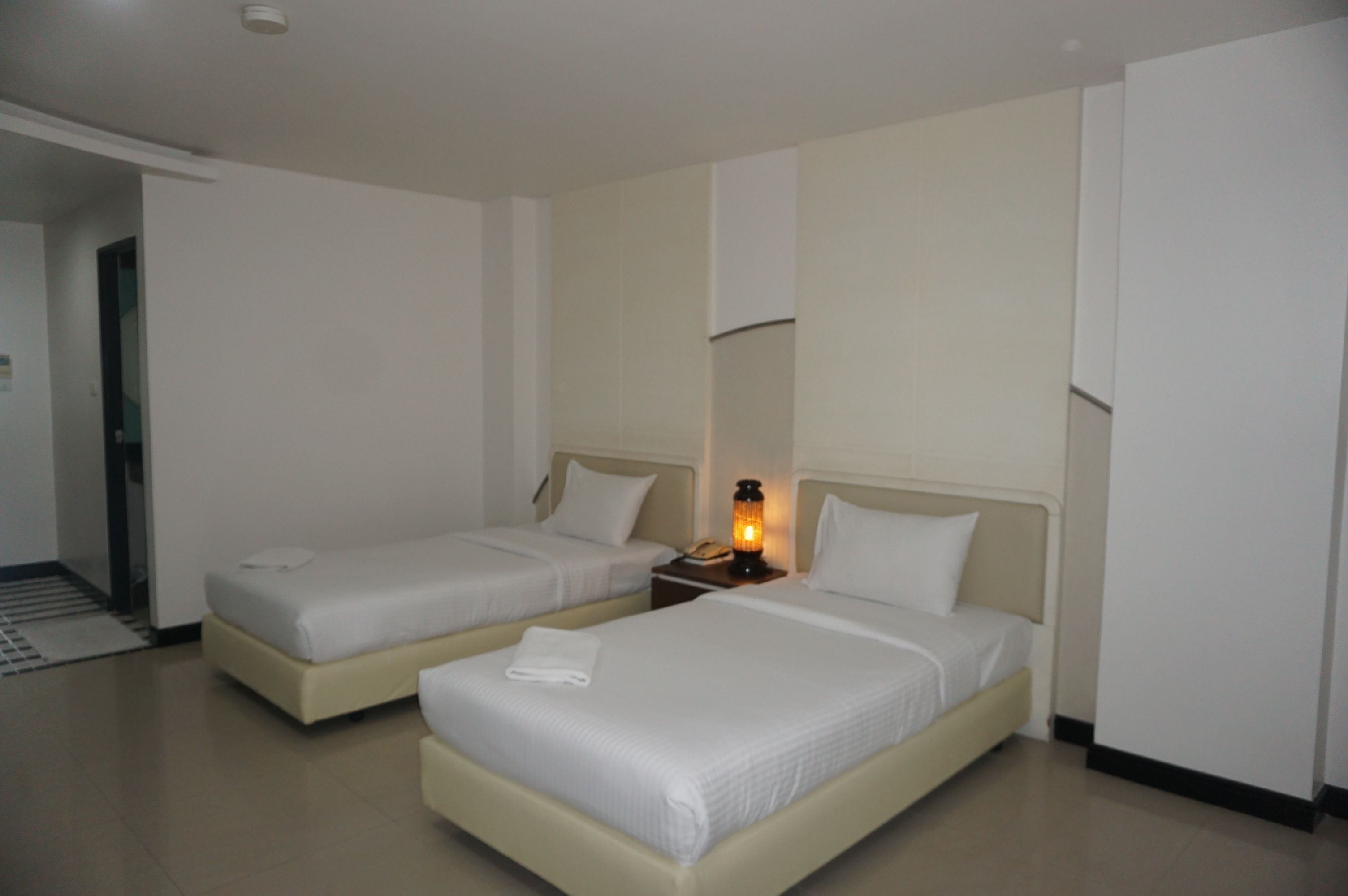 A hotel room with two beds, a nightstand with a lamp, and a door leading to a hallway.
