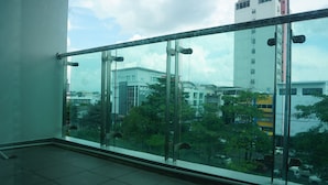 Un balcón con barandilla de cristal que da a una vista panorámica de la ciudad, con edificios y árboles.