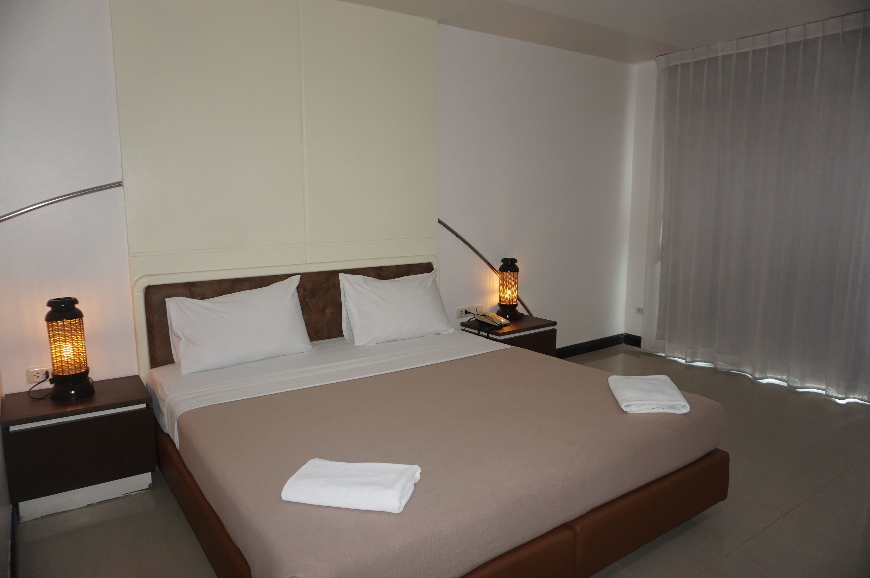Ein Hotelzimmer mit einem großen Bett, zwei Nachttischen mit Lampen und einem Fenster mit Vorhängen.