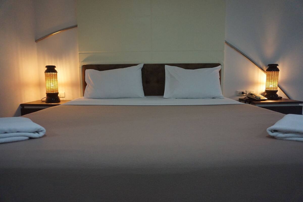 Ein ordentlich bezogenes Bett mit weißen Bettwäsche und je einer Nachttischlampe an jeder Seite.